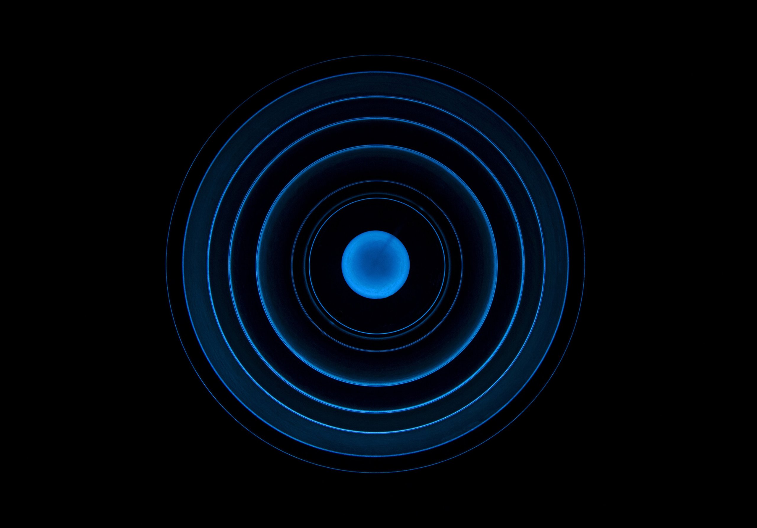 A hypnotic image with a bright blue sphere at the center, surrounded by glowing blue rings against a black background. It’s abstract and radiant.